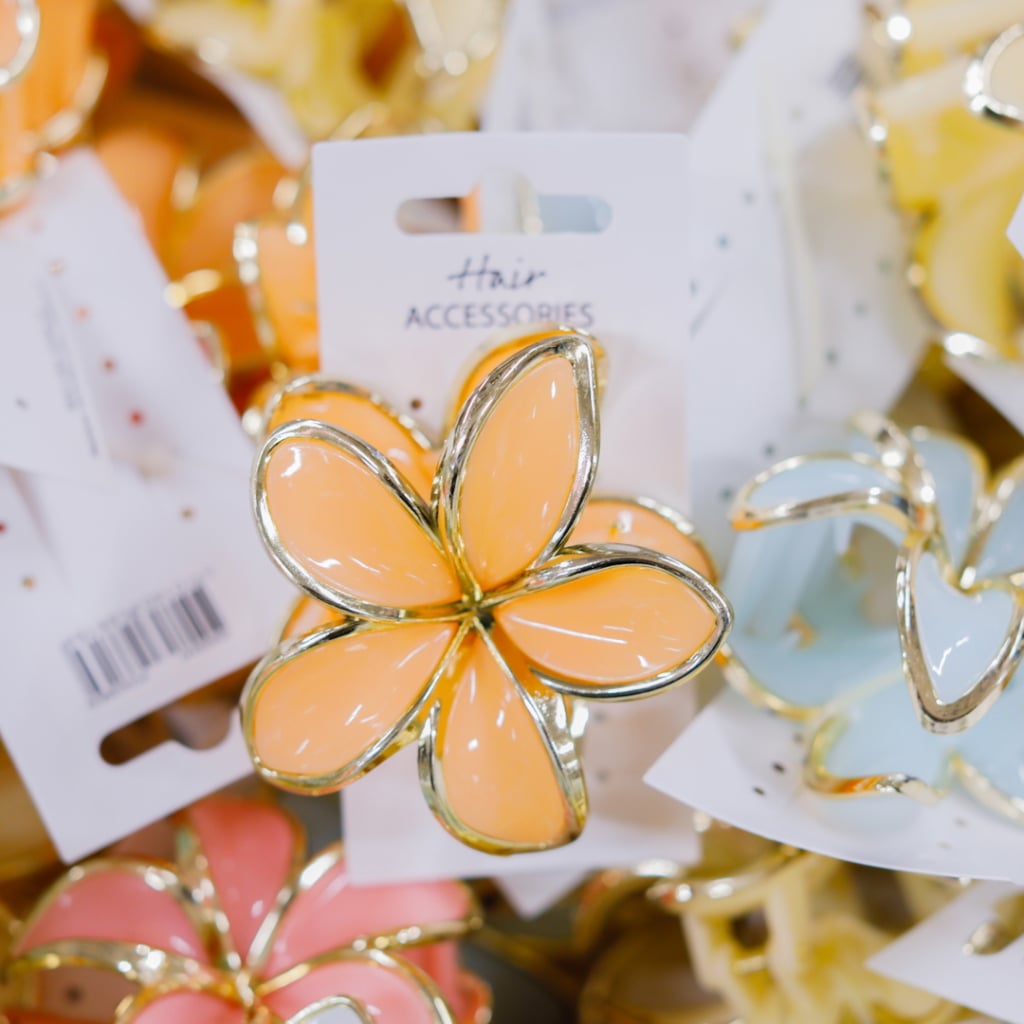 Färgglad håraccessoar i form av en blommig klämma med guldkanter, omgiven av flera andra liknande accessoarer i olika färger.