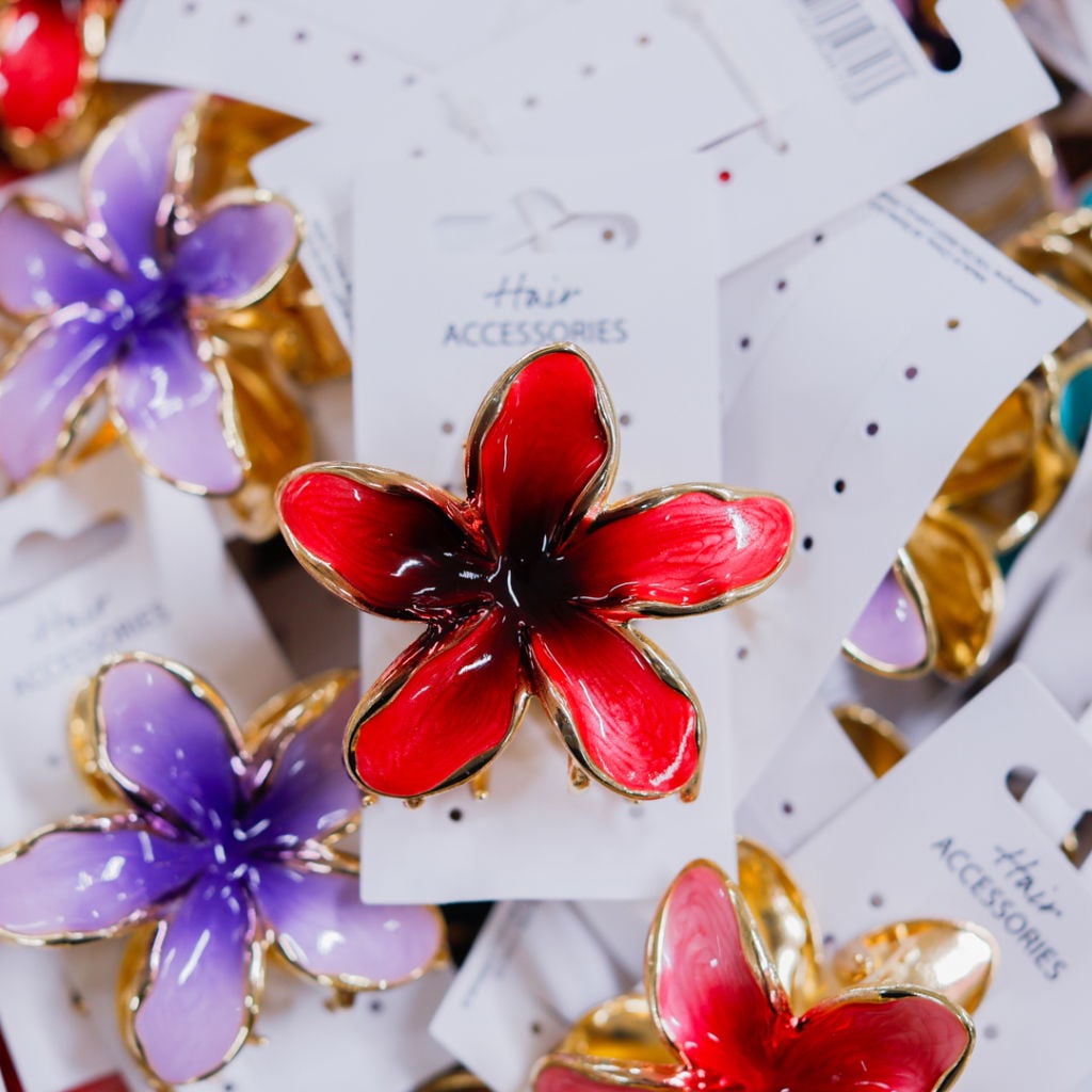 Färgglada håraccessoarer i form av blommor, inklusive en röd och en lila blomma, med guldkant och prislappar i bakgrunden. Perfekta för att styla hår och ge en elegant touch.