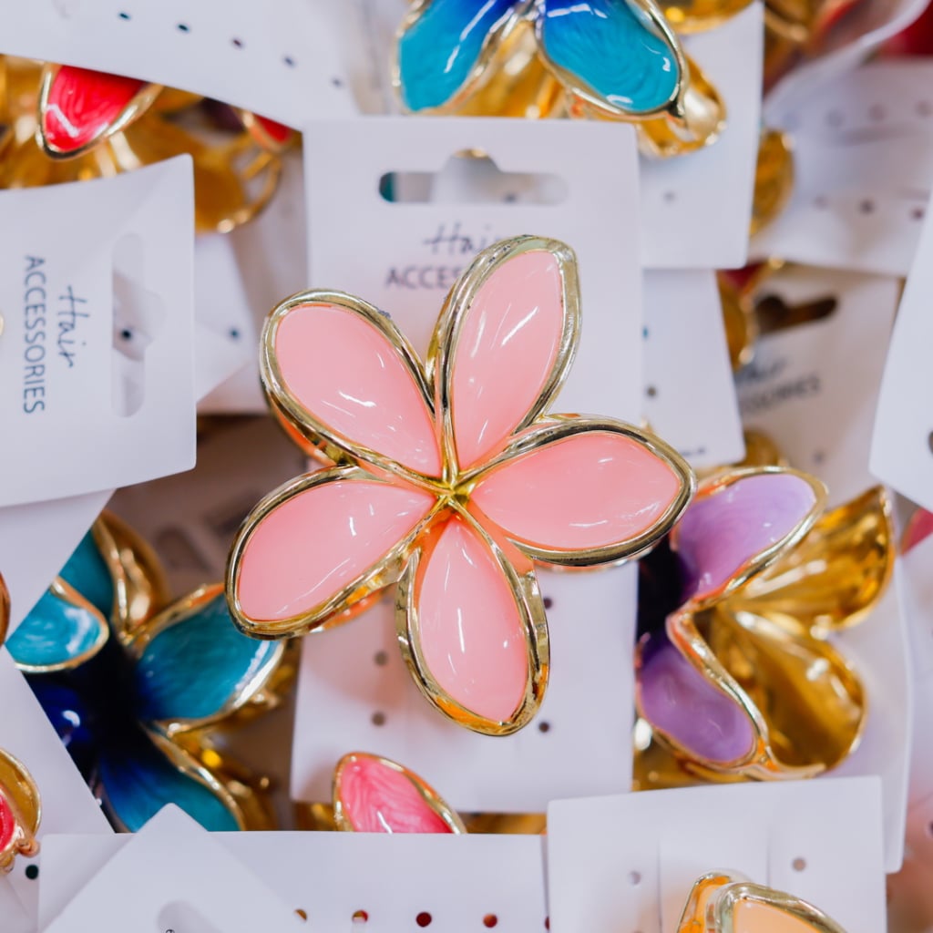 Färgglada håraccessoarer i form av blommor, med en stor rosa blomma i fokus omgiven av mindre blommor i blått, rött och lila, alla med gyllene detaljer.