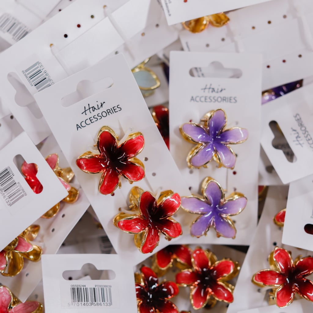 Flera färgglada håraccessoarer i form av blommor, inklusive röda och lila, förpackade på kort med etiketten "Hair Accessories".