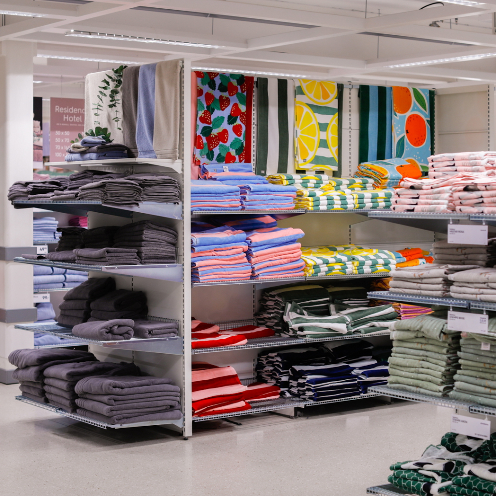 Färgglada handdukar och badlakan på hyllor i en butik, med olika mönster som jordgubbar, citrusfrukter och randiga designer.