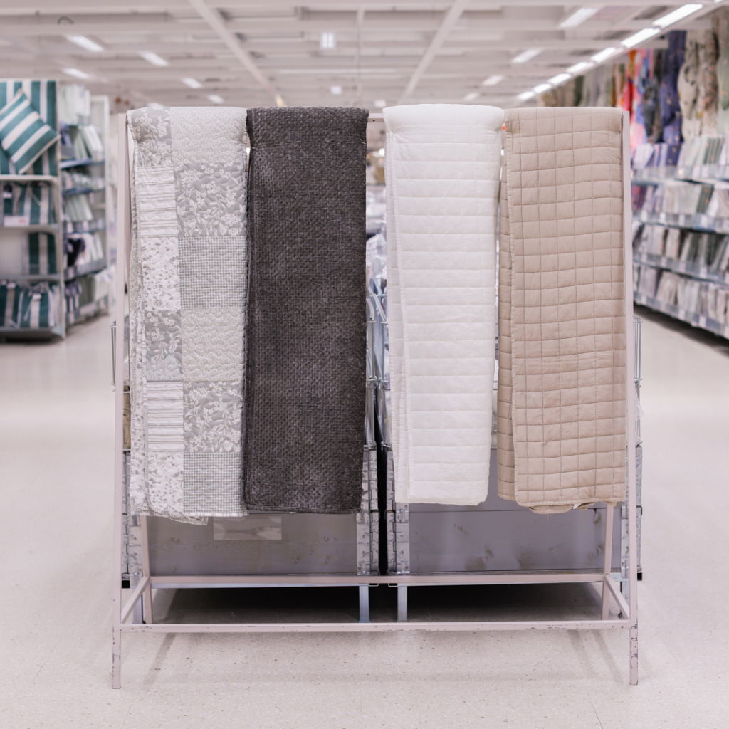 Fyra olika typer av sängkläder i en butik, inklusive mönstrat, mörkt och två neutrala färger, hängande på en ställning.