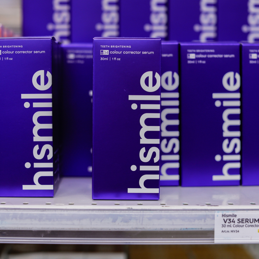 Lila förpackningar av Hismile V34 färgkorrigeringsserum för tandblekning, 30 ml, placerade på en hylla i en butik.