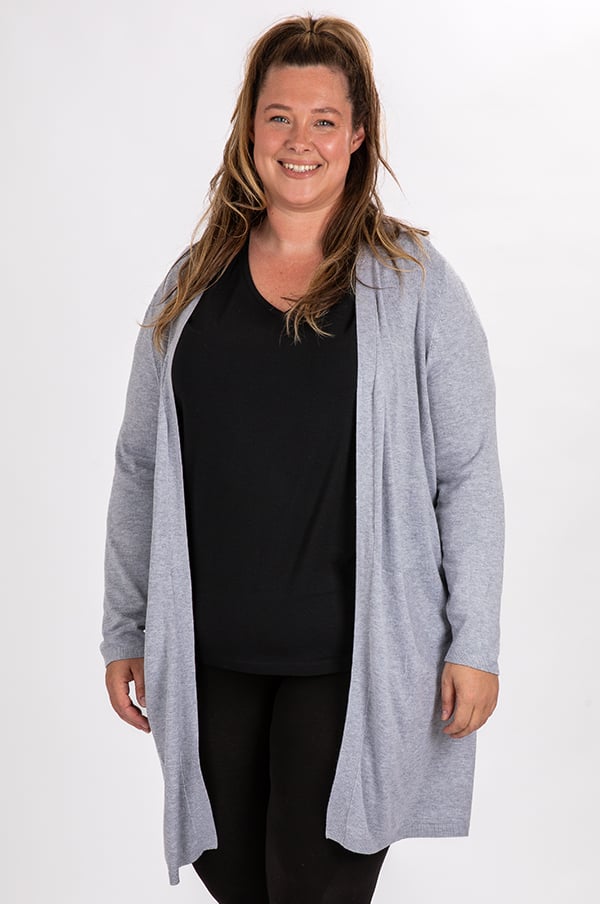 Glad kvinna i grå kofta och svart t-shirt, poserar framför en vit bakgrund. Idealisk för att visa upp avslappnad mode och plus size kläder.