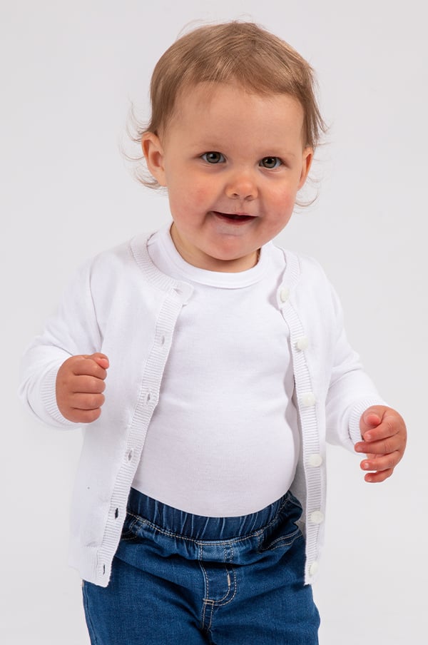Litet barn i vit kofta och jeans, leende mot kameran, på vit bakgrund.