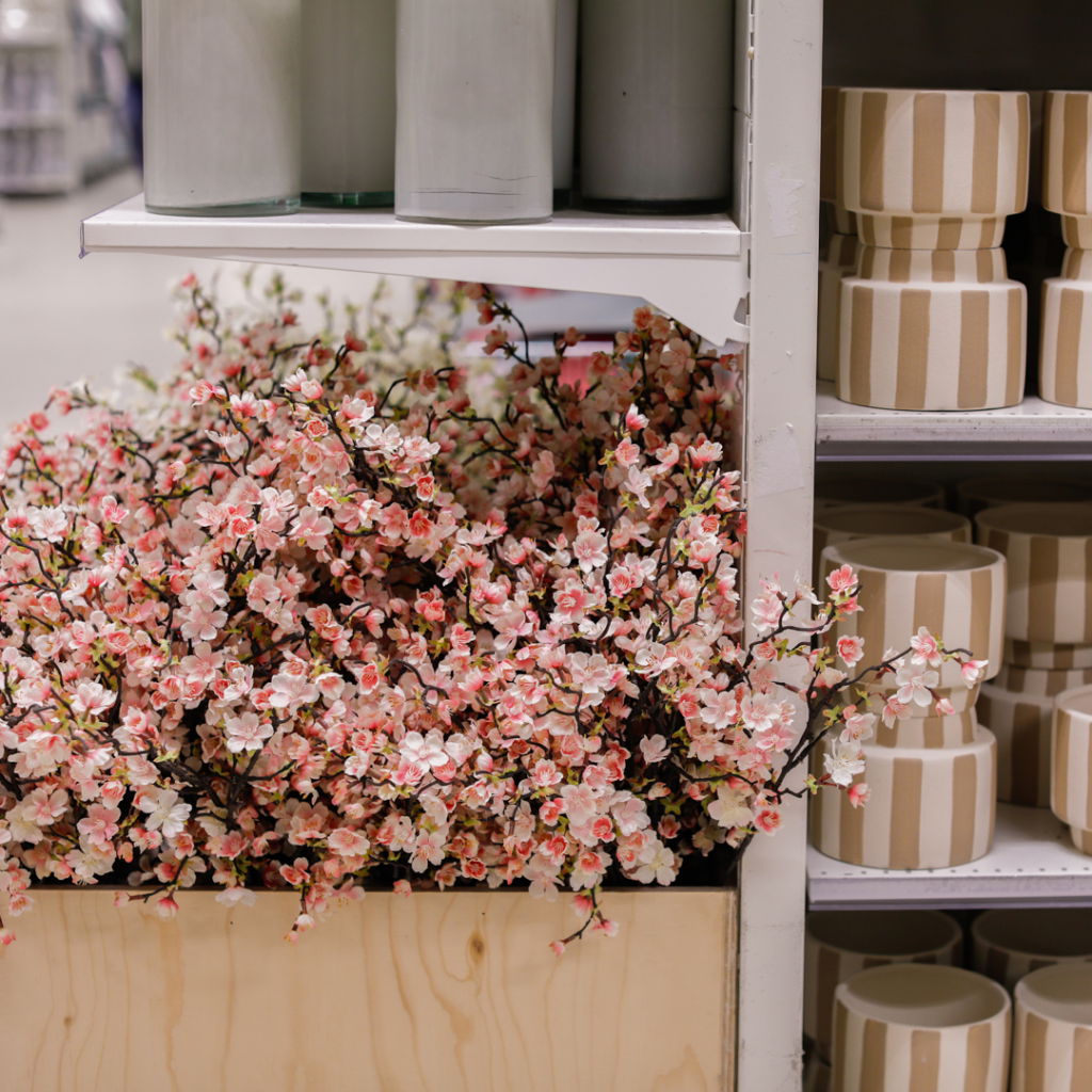 Vacker bukett med rosa konstblommor i en träkorg, omgiven av dekorativa krukor i olika mönster. Perfekt för inredning och blomsterarrangemang.