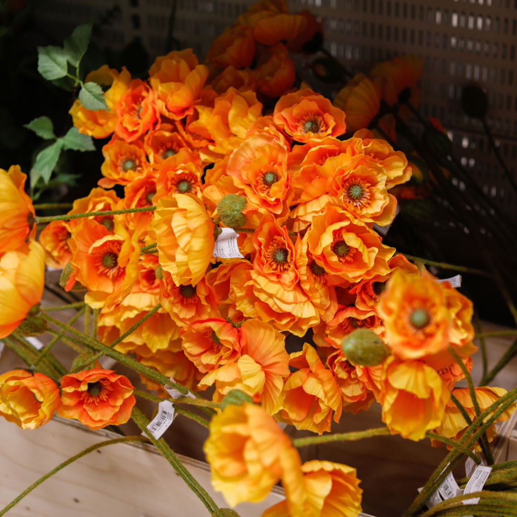 Färgglada konstgjorda blommor i orange och gult, arrangerade i en träbehållare, perfekta för inredning och dekoration.