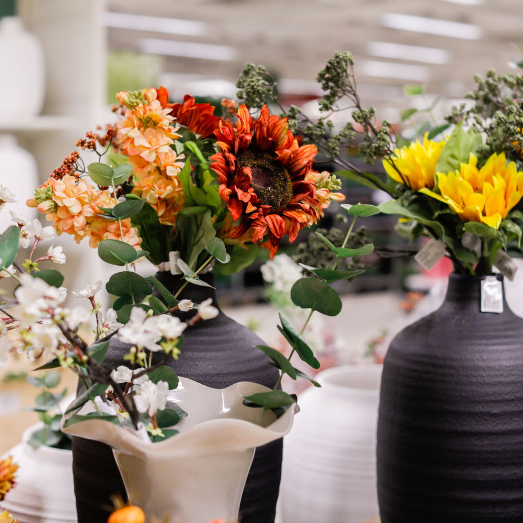 Vackra buketter med solrosor, orange blommor och gröna blad arrangemang i svarta och vita vaser, perfekt för inredning och dekoration.