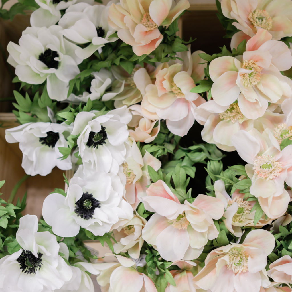 Vita och rosa konstgjorda blommor med gröna blad, arrangerade i en träbehållare, perfekt för dekoration och evenemang.