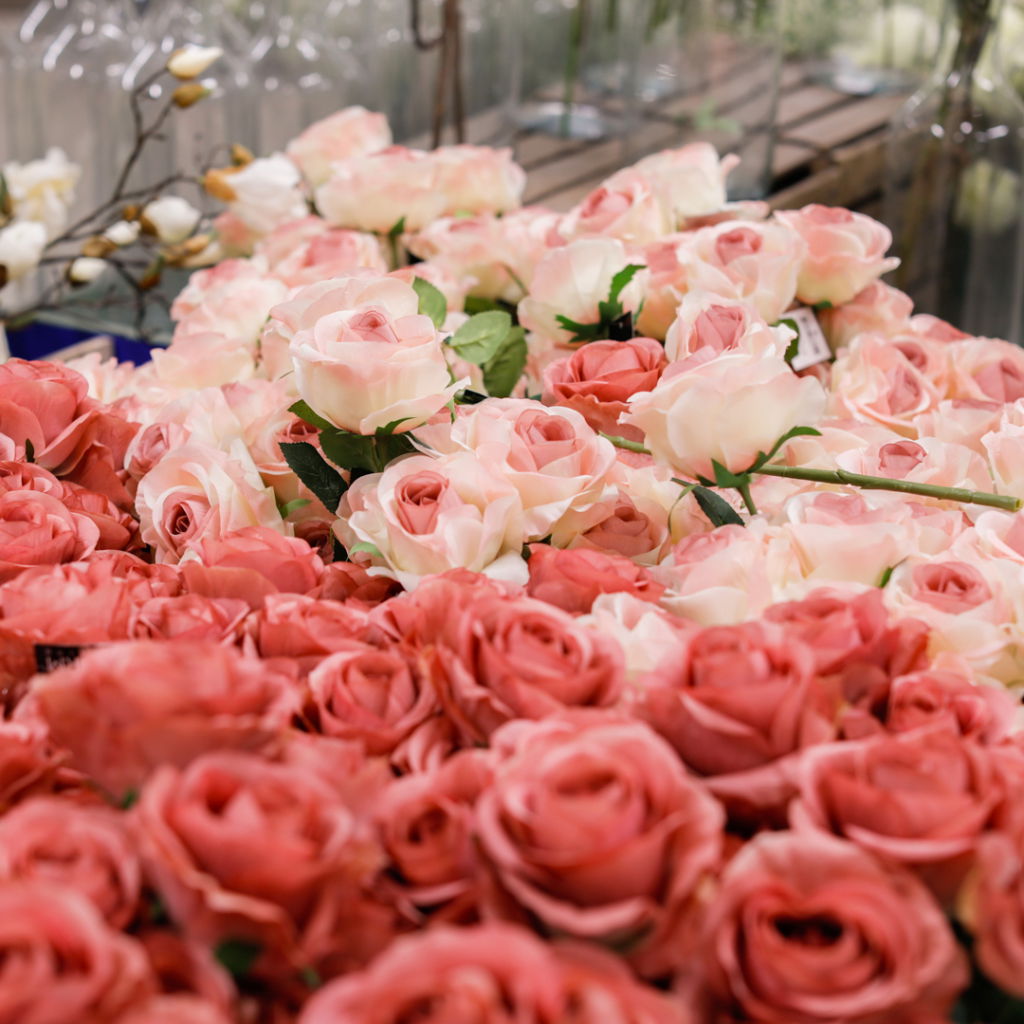 Färgglada rosor i olika nyanser av rosa och röd, arrangerade i en blomsterbutik. Blommorna är fräscha och prydligt placerade, vilket skapar en inbjudande atmosfär för kunder.