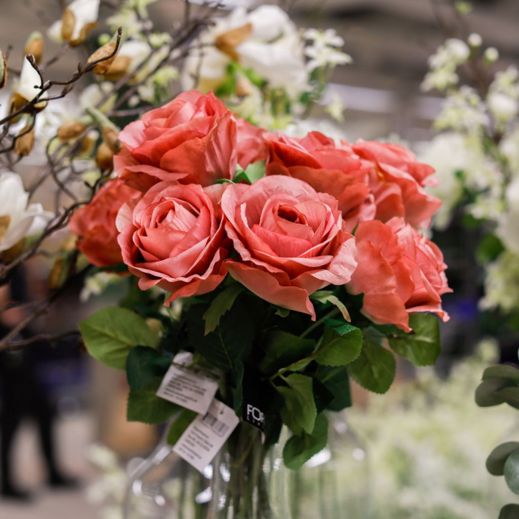 En bukett med rosa rosor omgiven av gröna blad och andra blommor, placerad i en glasvas, som skapar en vacker och livfull inredning.