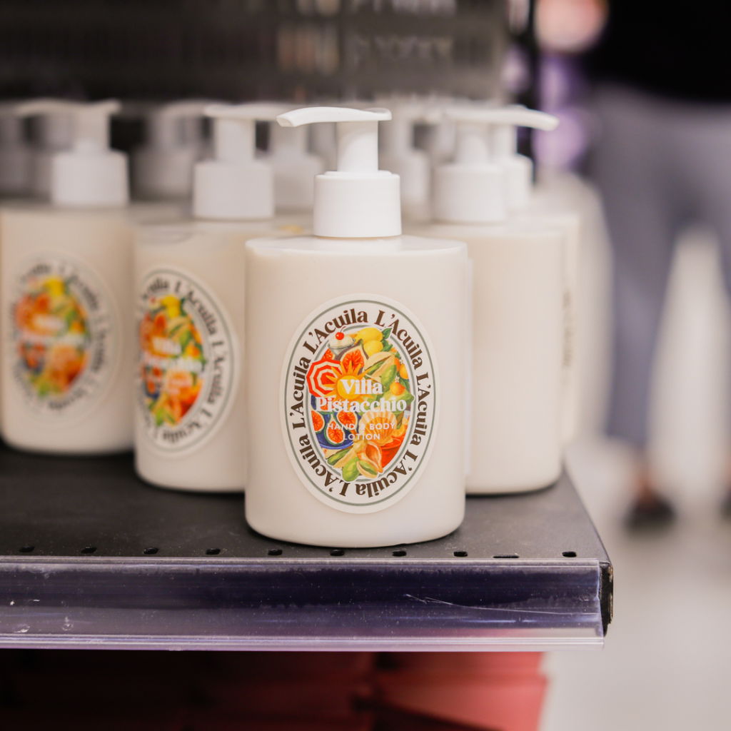 Flaska med hand- och kroppslotion från Villa Pistacchio, med färgglad etikett och pumpdispenser, placerad på en hylla i en butik.