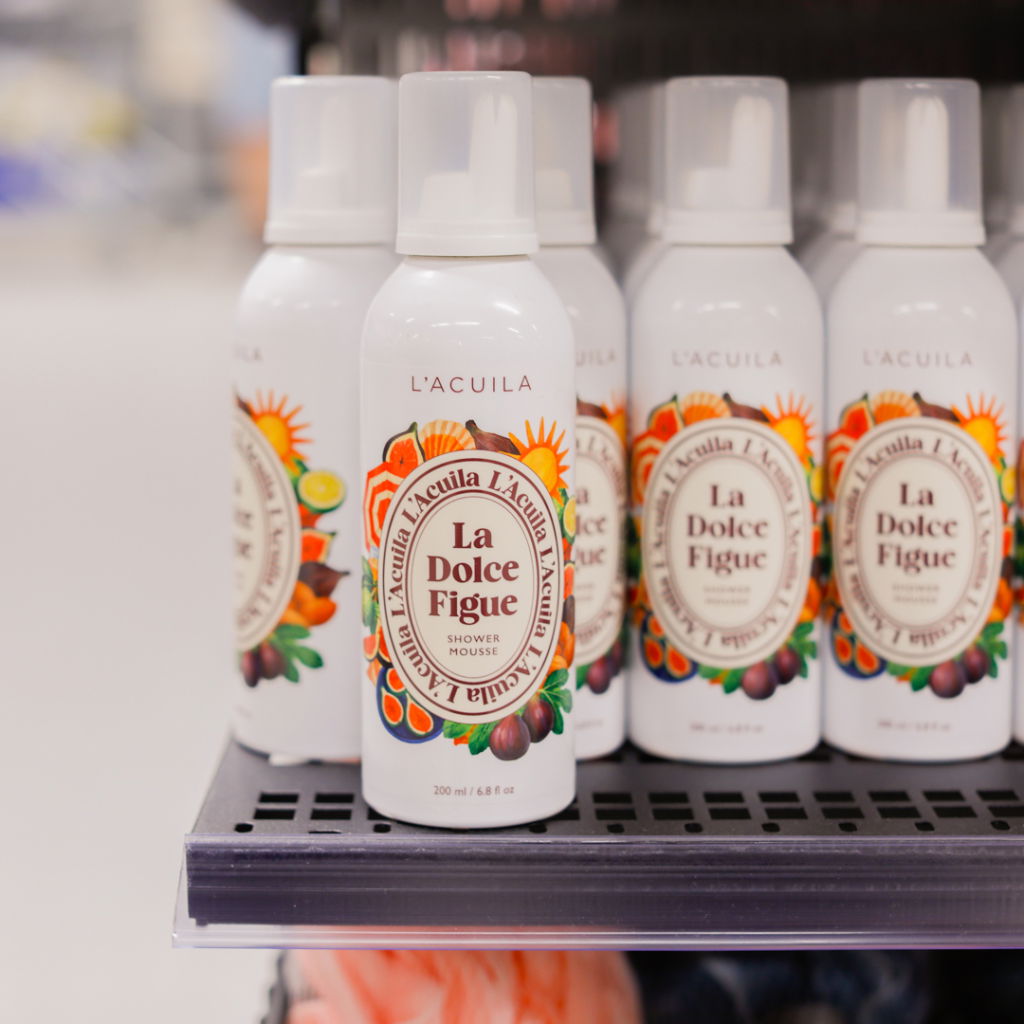 Flaskor med duschmousse från L'Acuìla, produktnamn "La Dolce Figue", som står på en hylla i en butik. Varje flaska innehåller 200 ml och har en färgglad design med fruktemblem.