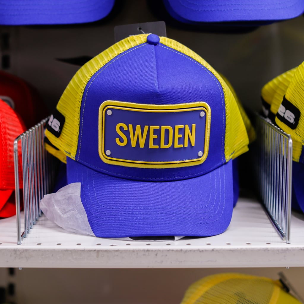 Blå och gul keps med texten "SWEDEN" på framsidan, placerad på en hylla bland andra färgglada kepsar. Perfekt för att visa stöd för Sverige.