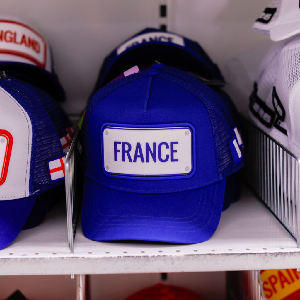 Blå keps med texten "FRANCE" på framsidan, bland andra kepsar i en butikshylla.