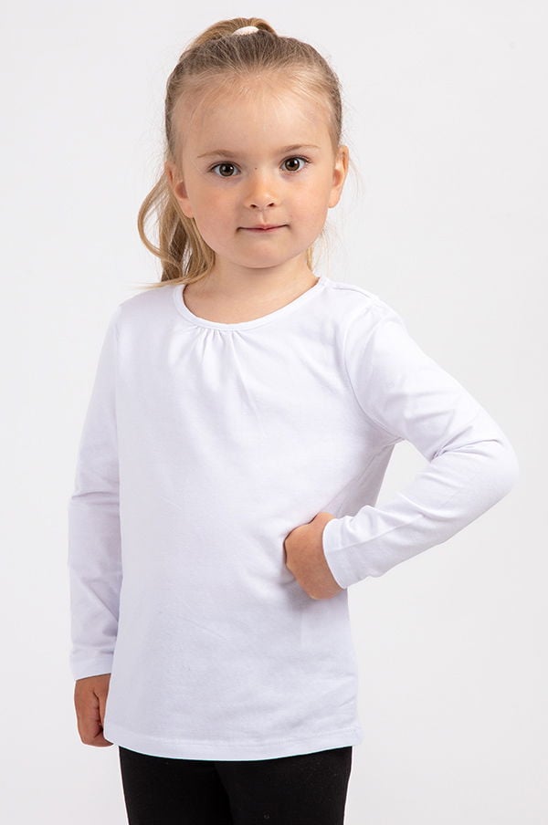 Liten flicka med långt hår i hästsvans, iförd en vit långärmad tröja, poserar med ena handen på höften.