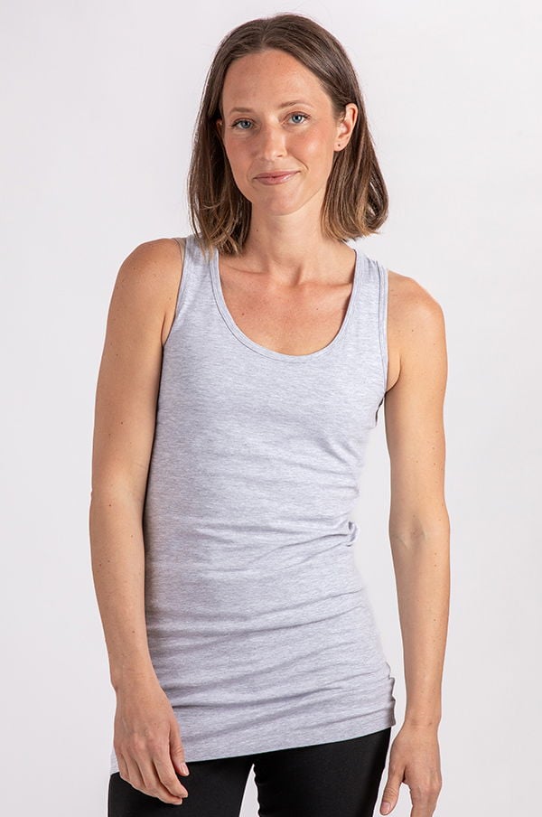 Kvinna som poserar i en grå ärmlös topp, med naturlig makeup och avslappnad frisyr, mot en ljus bakgrund. Perfekt för att illustrera sportkläder eller avslappnad mode.