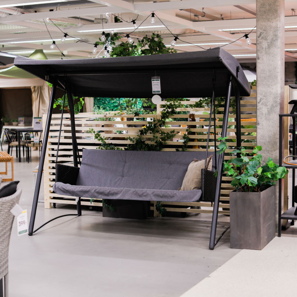 Svart hängsoffa med tak i en modern inredningsbutik, omgiven av grönska och dekorativa element, perfekt för utomhusbruk.