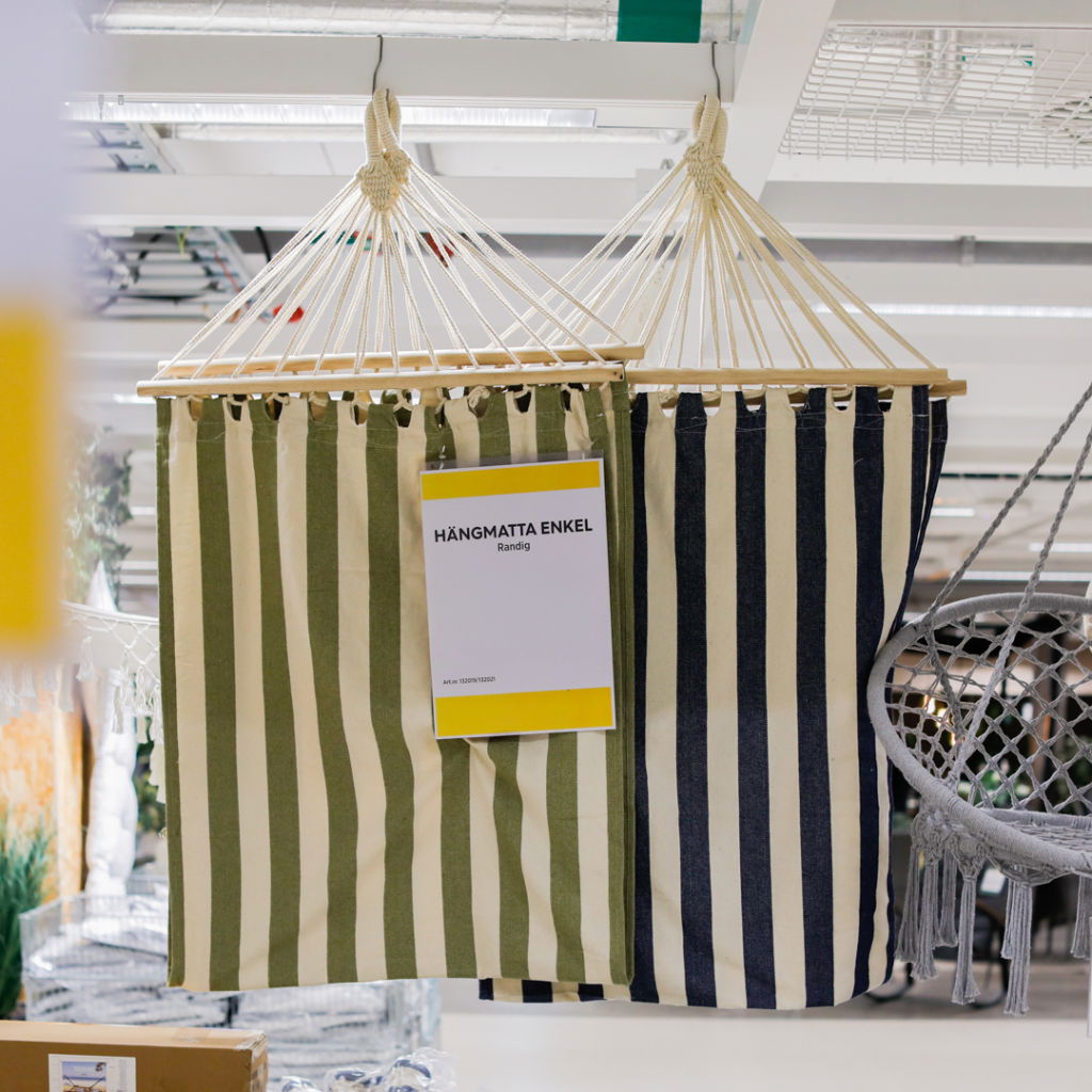 Hängmatta i randig design, tillgänglig i gröna och mörkblå färger, hängande i en butiksmiljö med produktinformation synlig.