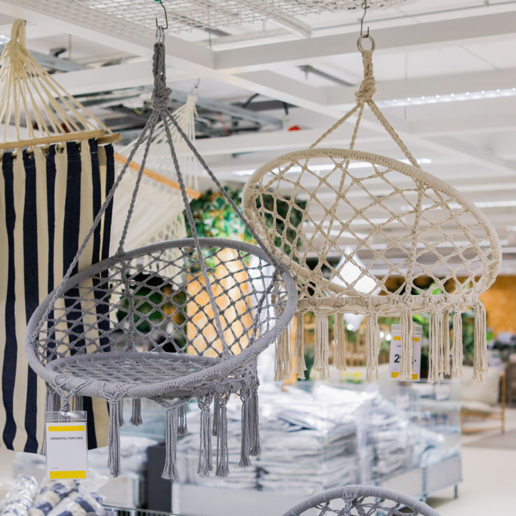 Hängande stolar i makramé, en grå och en beige, i en modern butiksmiljö. Stolarna är designade för både inomhus- och utomhusbruk och erbjuder en trendig sittlösning.