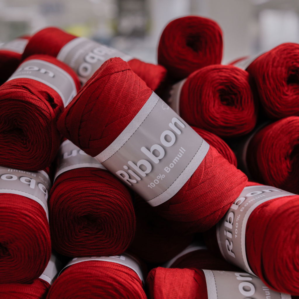 Röda garnrullar i 100% bomull med etikett som visar varumärket "Ribbon". Garnet är perfekt för hantverk och stickning.
