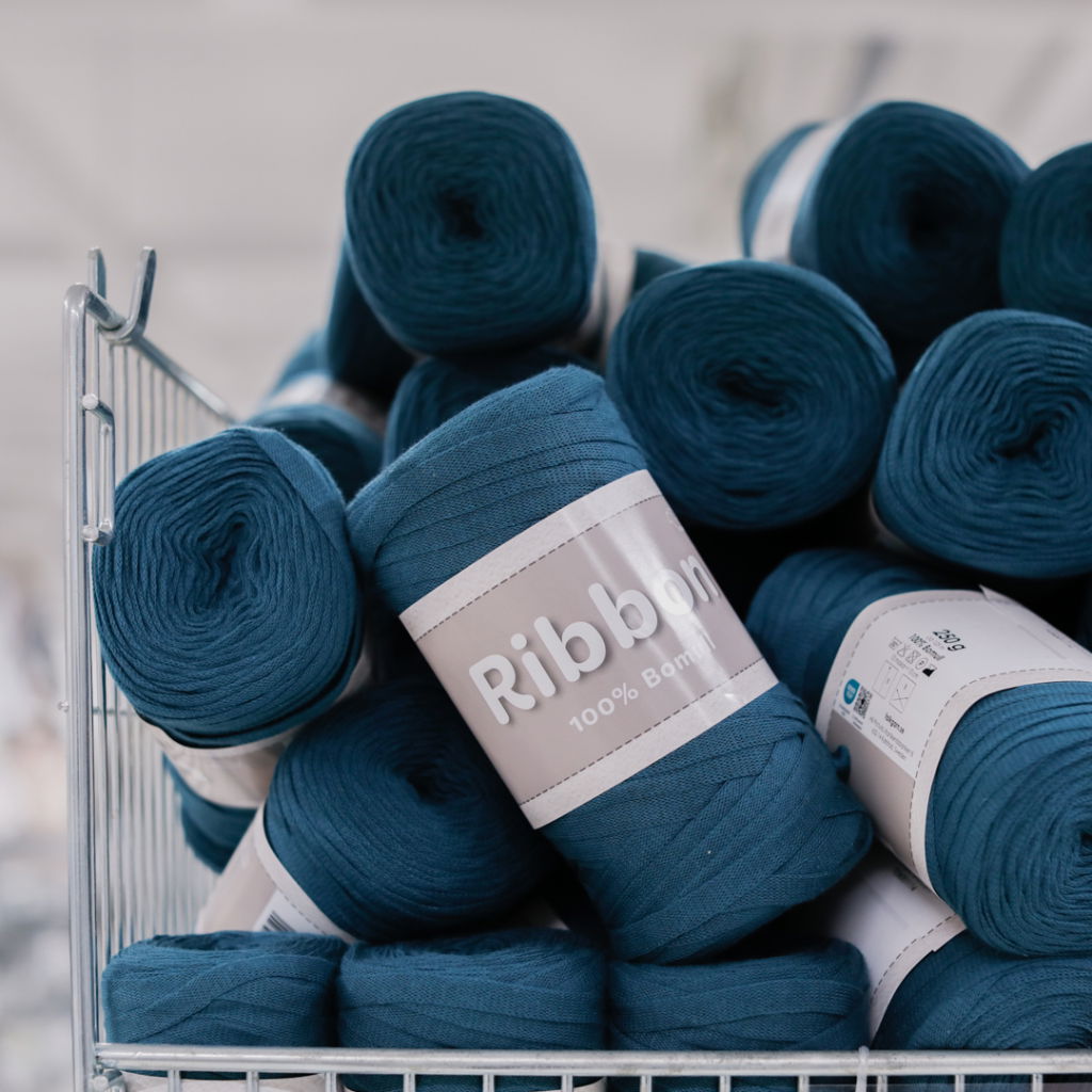 Rullar av blått bomullsgarn i en trådback, märkta med "Ribbon 100% Bambu", perfekta för hantverk och DIY-projekt.