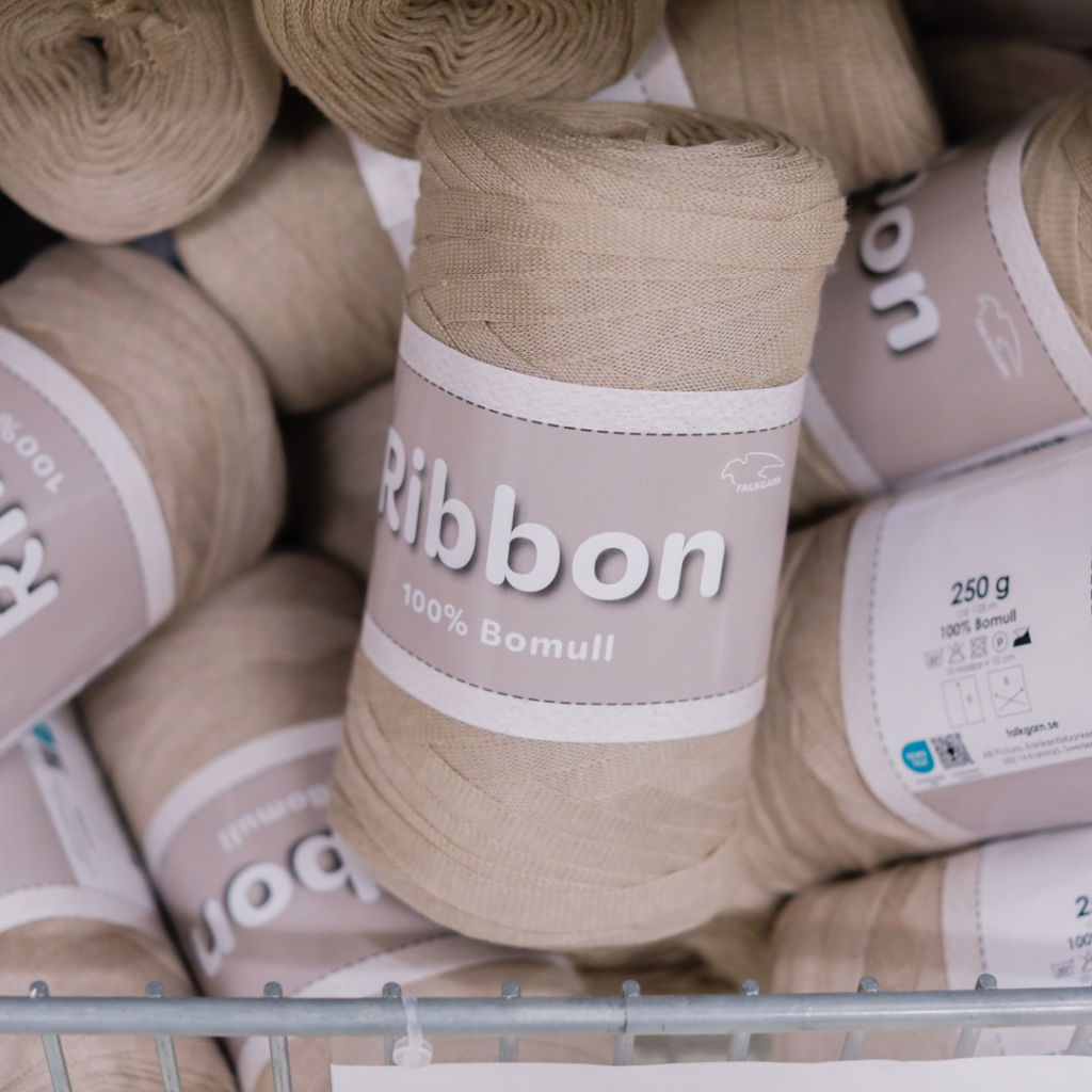Rullarna av bomullssnöre i beige färg, märkta med "Ribbon 100% Bomull" och vikt på 250 g, staplade i en korg. Perfekt för hantverk och DIY-projekt.