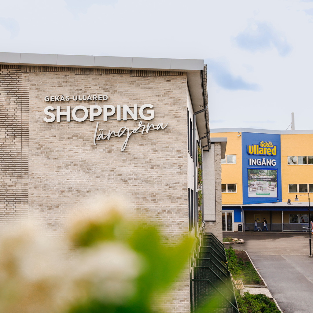 Gekås Ullared shoppingcenter med skyltar för shopping och ingång, omgiven av grönska.