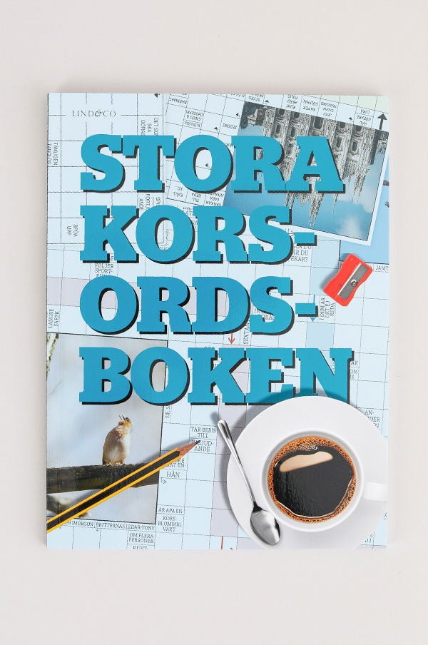 Stora korsordsboken med en kopp kaffe, en sked och en blyertspenna på ett bakgrund av korsord och bilder.