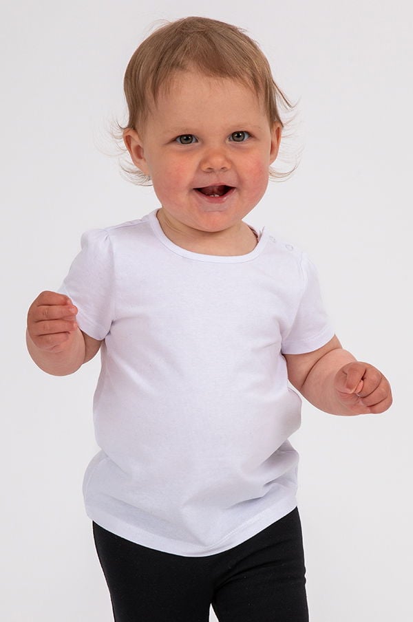 Litet barn med korta ärmar i vit t-shirt och svarta leggings, ler och står upp, på en neutral bakgrund.