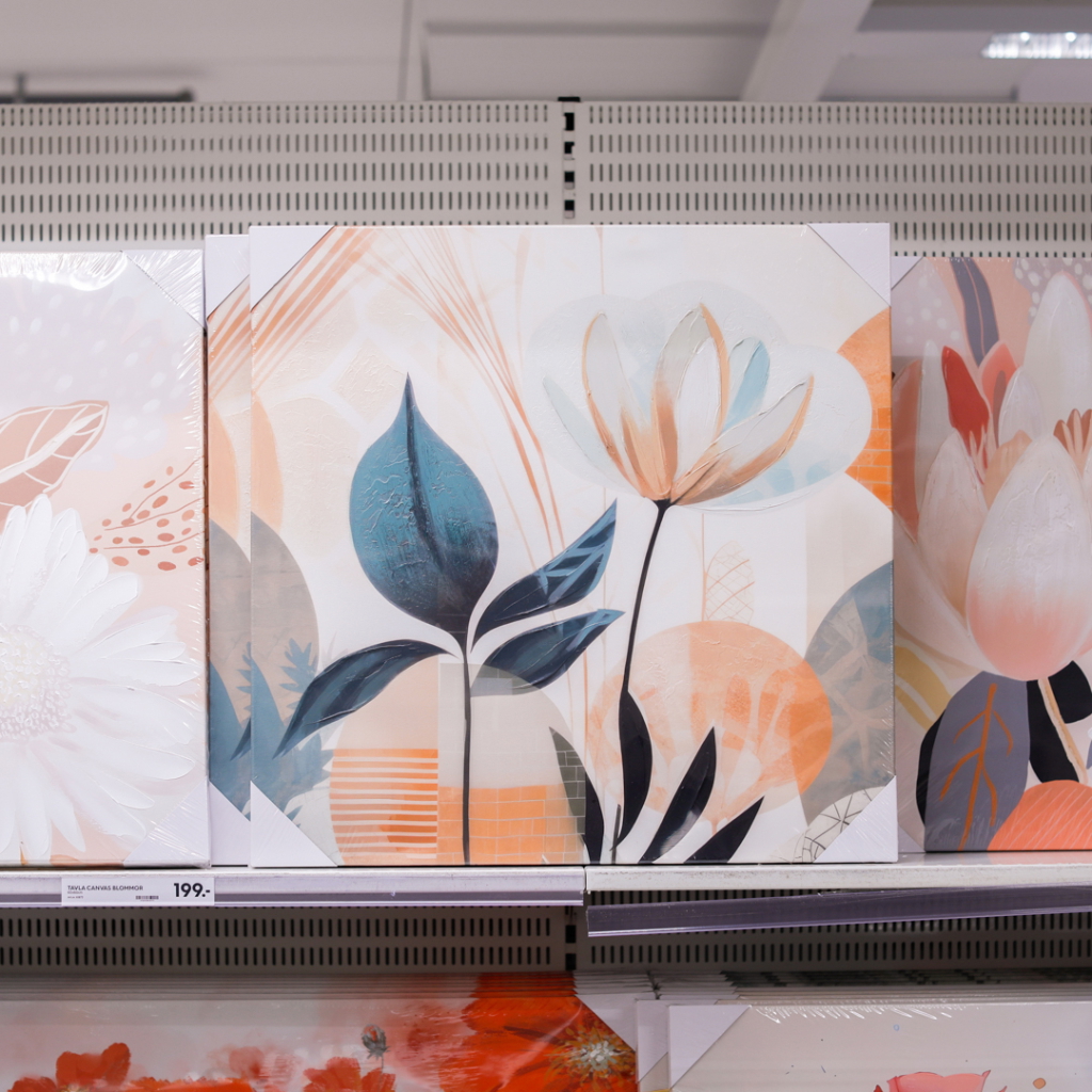 Konstverk med blommotiv i pastellfärger, inklusive tulpaner och gröna blad, utställd på en hylla i en butik.