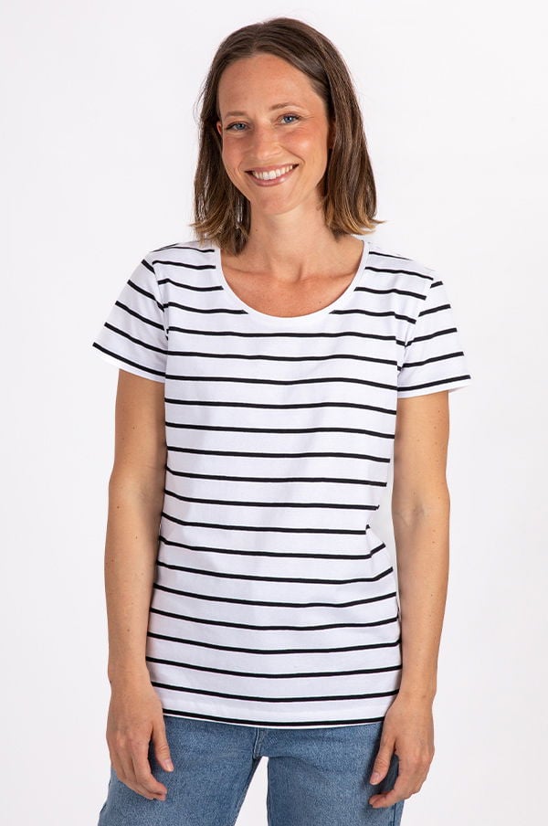 Kvinna i randig t-shirt med korta ärmar, leende mot kameran, stående framför vit bakgrund. T-shirten har svarta och vita ränder och kombineras med blå jeans. Idealisk för en avslappnad stil.