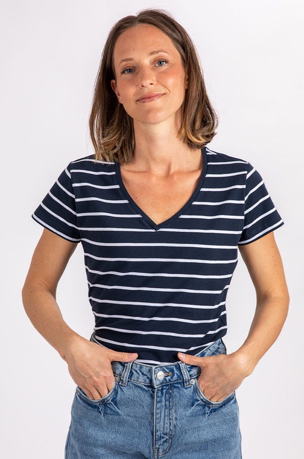 Kvinna bär en marinblå och vit randig t-shirt med V-hals, poserar med händerna i fickorna på sina jeans.