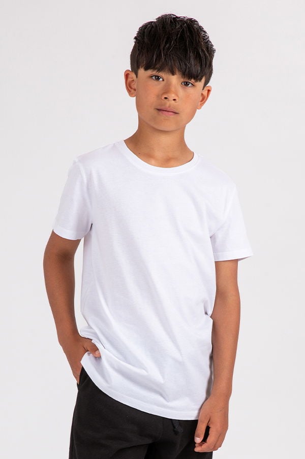 Porträtt av en ung pojke i vit t-shirt och svarta byxor, stående med en avslappnad pose mot en ljus bakgrund.