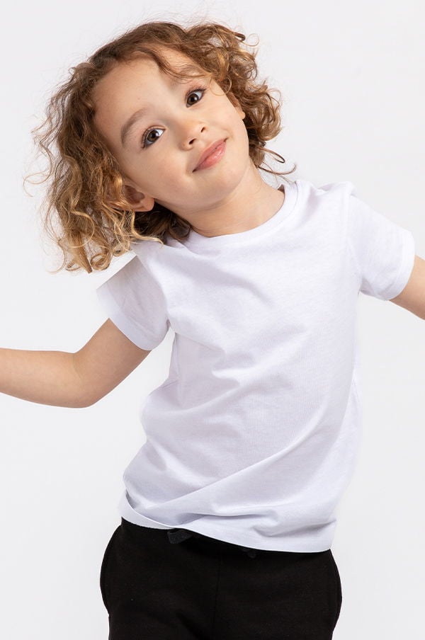 Barn med lockigt hår som poserar i en vit t-shirt och svarta byxor på vit bakgrund.