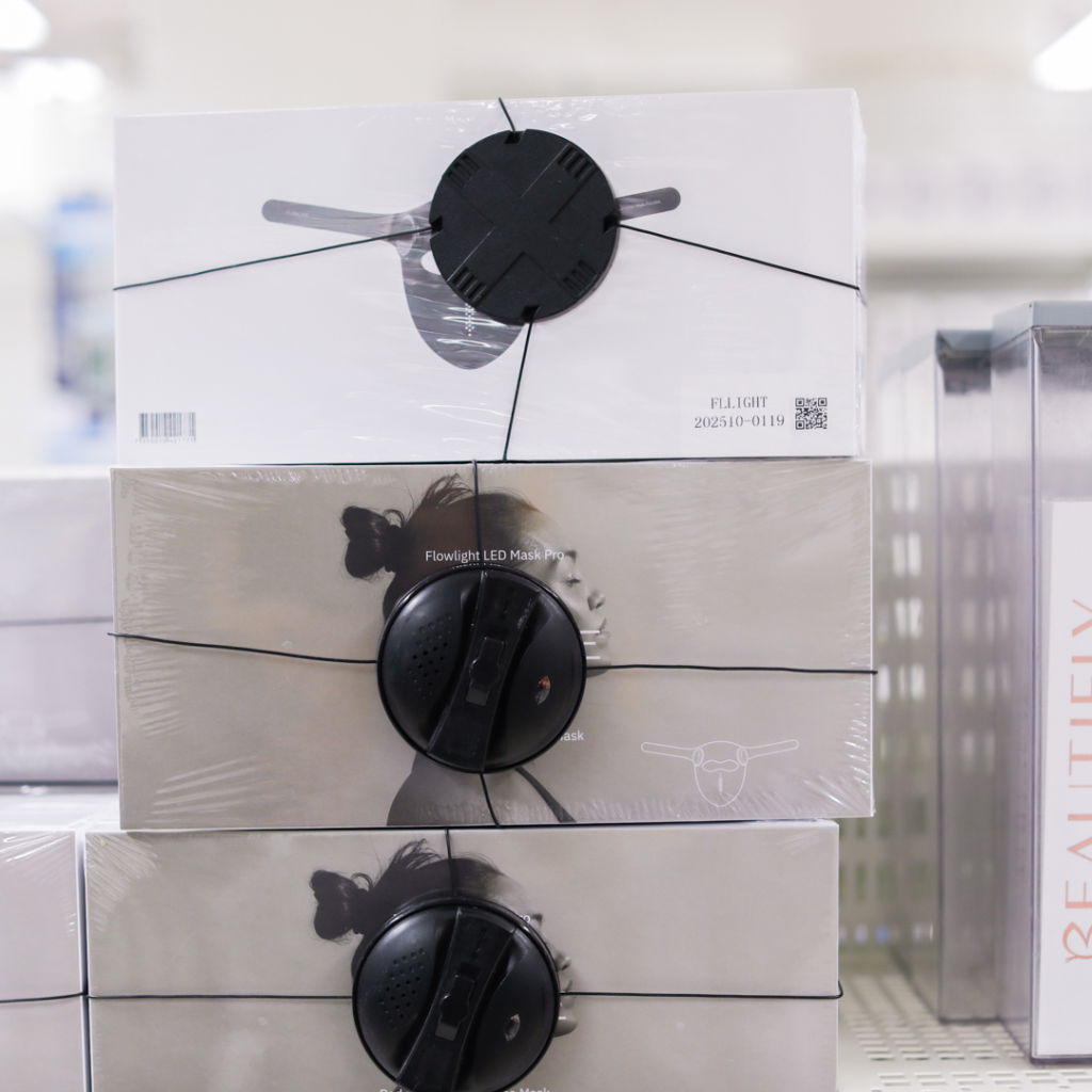 Packade Flowlight LED-masker staplade på en hylla i en butik, med tydlig produktinformation och lås på förpackningarna.