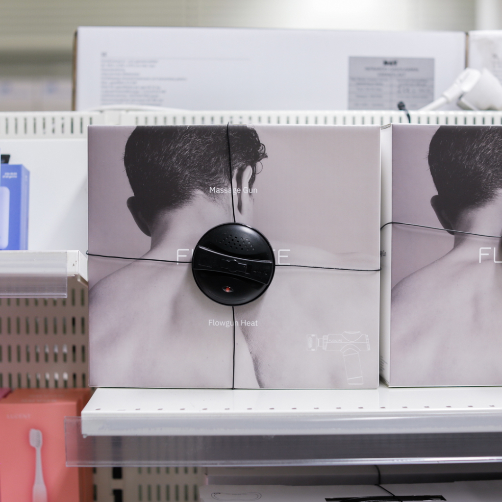 Förpackning av en massagepistol med värmefunktion, placerad på en hylla i en butik. Produkten är designad för muskelavslappning och återhämtning.
