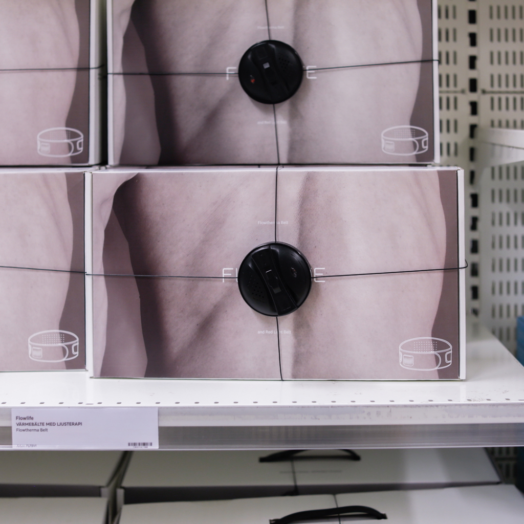 Förpackningar med Flowlife Flowtherma-bälte, som används för att lindra smärta och förbättra återhämtning, placerade på hyllor i en butik.